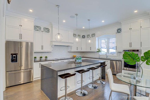 Picture8 - Toronto Bangla Town | Digital Bangla Weekly Magazine Bright white kitchen with a gray island, four bar stools, stainless fridge/oven, pendant lights, and a round glass dining table by a window.