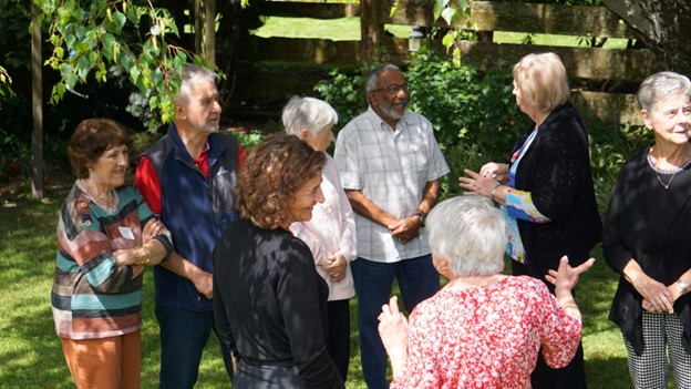 Picture1 - Toronto Bangla Town | Digital Bangla Weekly Magazine A group of older adults standing in a circle outdoors, talking and smiling in a sunny backyard.