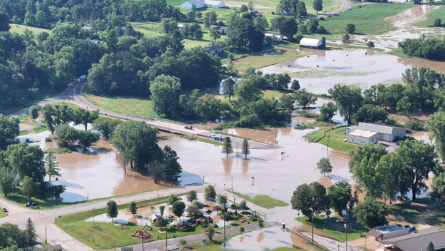 Picture3 - Toronto Bangla Town | Digital Bangla Weekly Magazine Aerial view of a rural area with floodwater covering roads, yards, and fields around homes and farms.