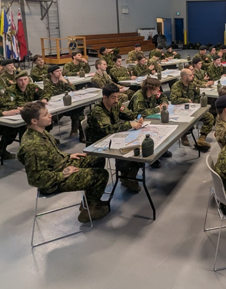 Picture4 - Toronto Bangla Town | Digital Bangla Weekly Magazine Group of soldiers in camouflage uniforms seated at long tables in a gym, studying maps and taking notes.