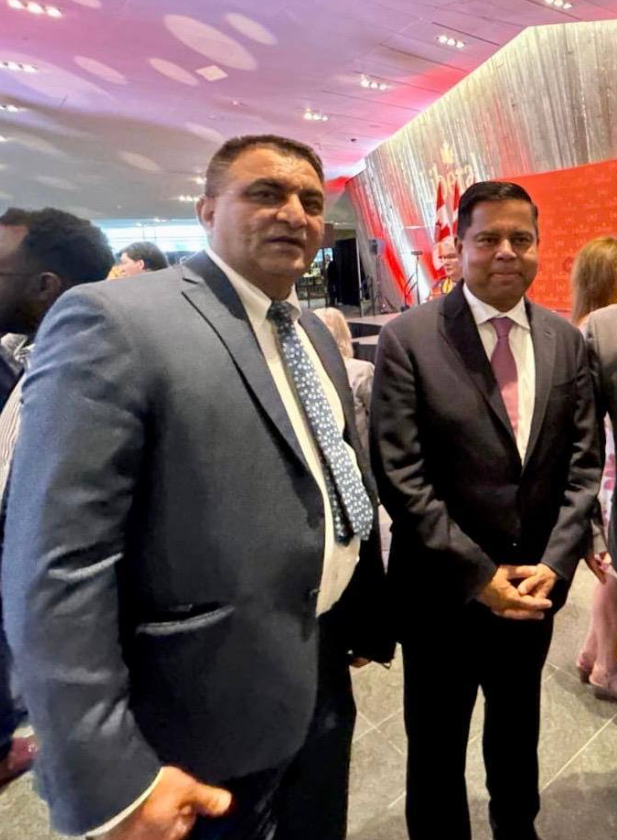 Picture4 - Toronto Bangla Town | Digital Bangla Weekly Magazine Two men in suits posing for a photo at a formal event, one in a light gray suit and polka-dot tie, the other in a dark suit with a pink tie.