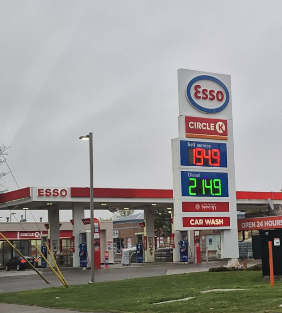 Picture5 - Toronto Bangla Town | Digital Bangla Weekly Magazine Tall digital price board at an Esso Circle K gas station showing self-serve price 1.949 and diesel 2.149 under an overcast sky.