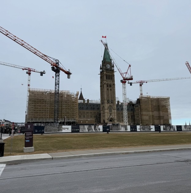 Picture5 - Toronto Bangla Town | Digital Bangla Weekly Magazine Parliament Hill in Ottawa under renovation with scaffolding, multiple cranes, and a Canadian flag atop the central tower.
