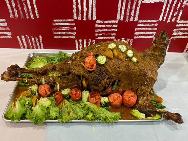 Picture6 - Toronto Bangla Town | Digital Bangla Weekly Magazine Whole roasted lamb presented on a metal tray with greens and carved tomato roses and cucumber slices as garnish.