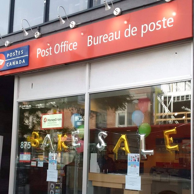 Picture7 - Toronto Bangla Town | Digital Bangla Weekly Magazine Canada Post office storefront with a red sign reading 'Post Office / Bureau de poste'; window displays yellow balloon letters spelling 'BAKE SALE' and a MoneyGram sign.
