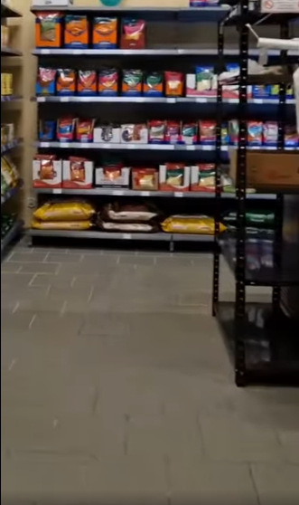 Picture9 - Toronto Bangla Town | Digital Bangla Weekly Magazine Store aisle with metal shelving stocked with bags of dry pet food on multiple shelves, colorful packaging visible on top rows.