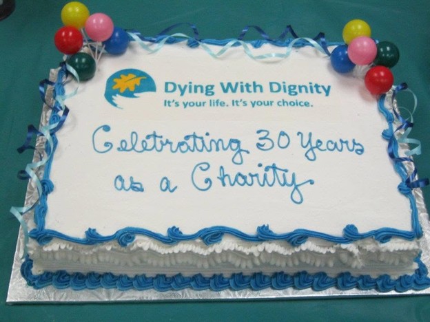 Picture10 - Toronto Bangla Town | Digital Bangla Weekly Magazine Celebration cake with blue icing, balloons on top, and a logo reading "Dying With Dignity"—"Celebrating 30 Years as a Charity".