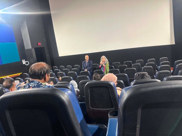 Picture12 - Toronto Bangla Town | Digital Bangla Weekly Magazine Audience seated in a dark theater watches two presenters on stage in front of a large screen behind them.