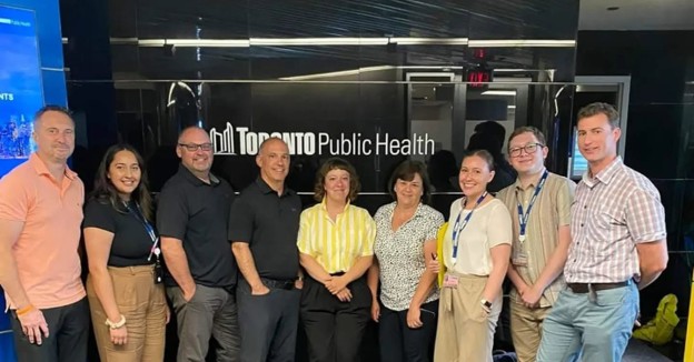 Picture4 - Toronto Bangla Town | Digital Bangla Weekly Magazine Ten professionals posing for a group photo in front of a Toronto Public Health sign.