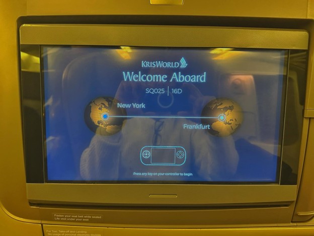 Picture5 - Toronto Bangla Town | Digital Bangla Weekly Magazine In-flight KrisWorld Welcome Aboard screen showing route from New York to Frankfurt with globe icons and a remote control image.