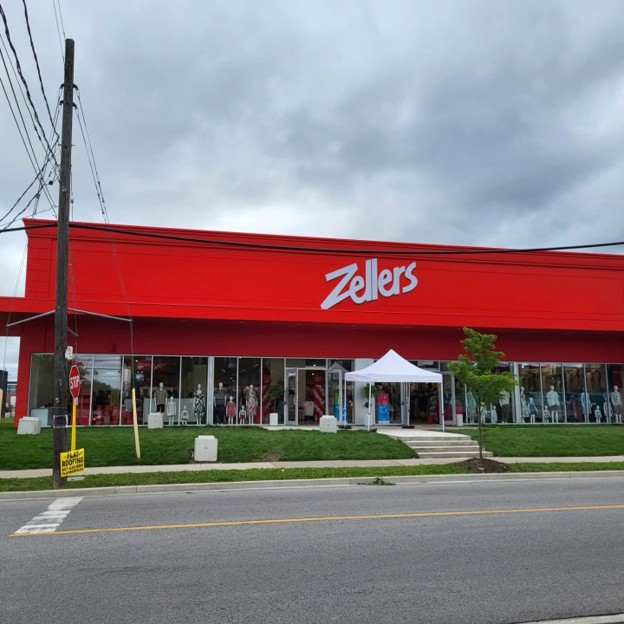 Picture6 - Toronto Bangla Town | Digital Bangla Weekly Magazine Red Zellers storefront with large glass windows displaying mannequins; white canopy tent outside and a small tree in front under a cloudy sky.