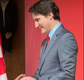 Picture6 - Toronto Bangla Town | Digital Bangla Weekly Magazine Man in a gray suit and red tie extends his hand for a handshake in front of a red backdrop (partial flag visible).