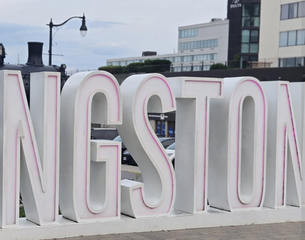 Picture9 - Toronto Bangla Town | Digital Bangla Weekly Magazine Large white 3D Kingston sign on a sidewalk with city buildings in the background.