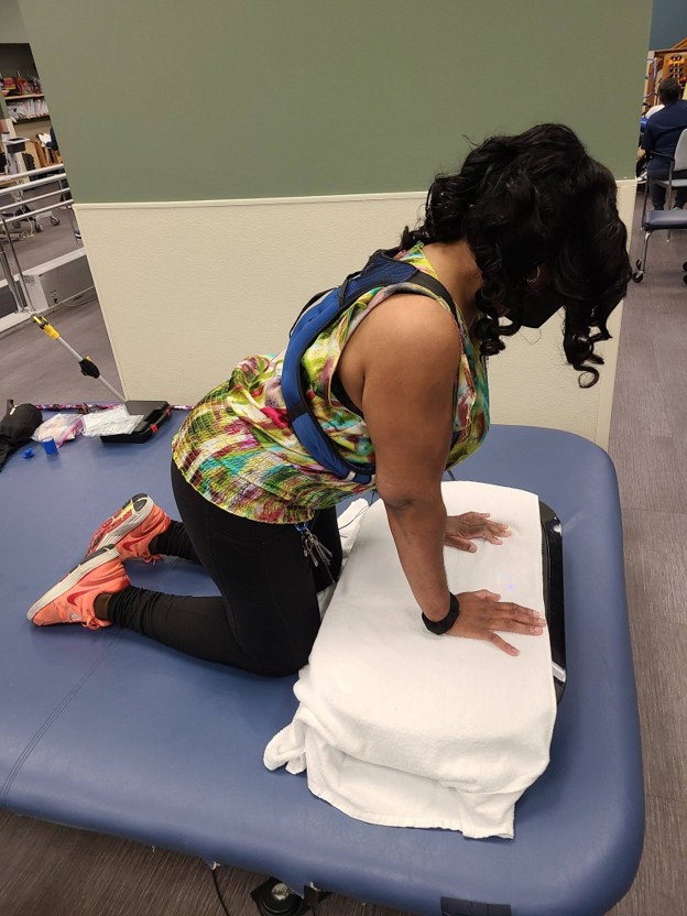 Picture10 - Toronto Bangla Town | Digital Bangla Weekly Magazine Woman kneeling on a blue padded therapy table, hands pressed on a folded towel as she performs a push-up-style exercise in a rehab/therapy setting