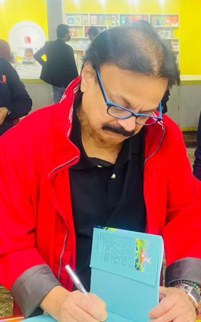 Picture11 - Toronto Bangla Town | Digital Bangla Weekly Magazine Man with blue glasses and a red jacket signs a light blue booklet at a counter in a bright store.