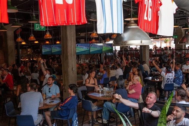 Picture2 - Toronto Bangla Town | Digital Bangla Weekly Magazine Busy sports bar with crowds at tables watching games on multiple screens; red jerseys hang from the ceiling above.