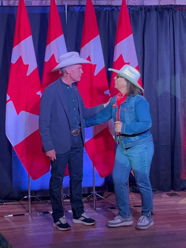 Picture3 - Toronto Bangla Town | Digital Bangla Weekly Magazine Two people in cowboy hats greet each other on a stage with Canadian flags behind them.