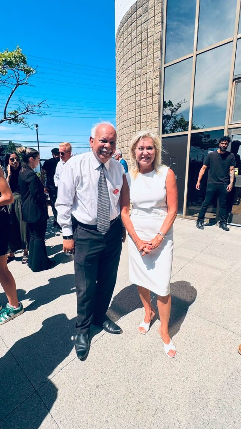 Picture4 - Toronto Bangla Town | Digital Bangla Weekly Magazine Two people in formal attire pose outside a modern glass-front building on a sunny day, smiling at the camera (man in white shirt and tie, woman in white dress).