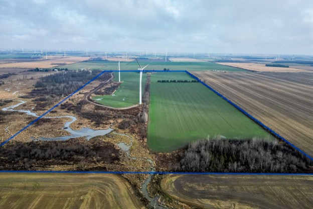 Picture4 - Toronto Bangla Town | Digital Bangla Weekly Magazine Aerial view of rural farmland with wind turbines on the horizon; a rectangular green field is outlined by blue lines, with a wetland and brown fields to the left and crops to the right.